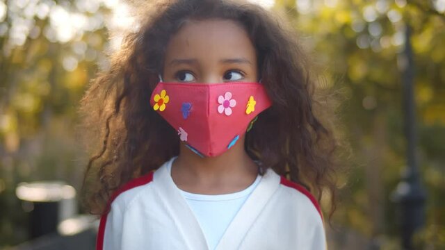 Portrait of small african girl with face mask standing outdoors