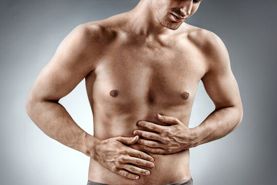 Man holding his stomach in pain. Photo of man with naked torso experience stomachaches on grey background. Medical concept
