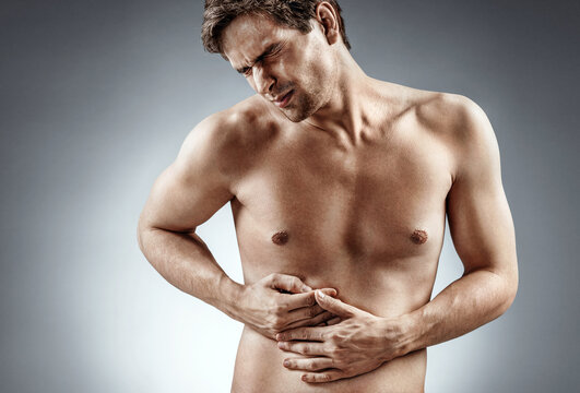 Diseased liver. Photo of man holding his hand in area liver and grimacing in pain on grey background. Medical concept