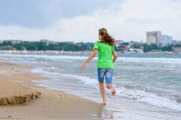 Fototapeta na wymiar A girl happily runs along the sea coast, view from the back
