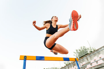 Fit female teenager athlete hurdler running jumping over hurdles - Bottom view