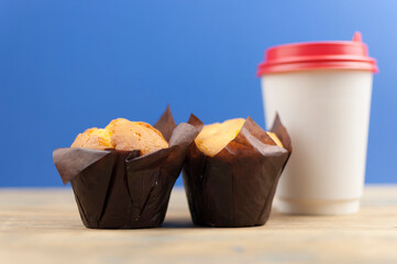 Classic banana nut muffins in black paper wrapper with disposable paper coffee cups on wooden table. Coffee time