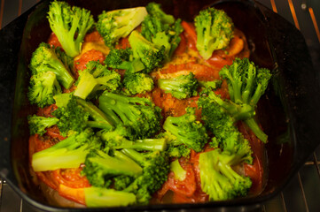 baked vegetables in the oven. Pieces of broccoli, tomato are in the oven in yellow light. Concept of cooking healthy food.