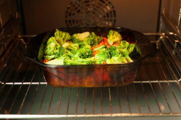 baked vegetables in the oven. Pieces of broccoli, tomato are in the oven in yellow light. Concept of cooking healthy food.