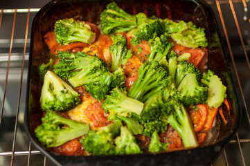 baked vegetables in the oven. Pieces of broccoli, tomato are in the oven in yellow light. Concept of cooking healthy food.
