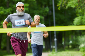Two active sporty senior men finishing running marathon race with bearded man being first, medium...