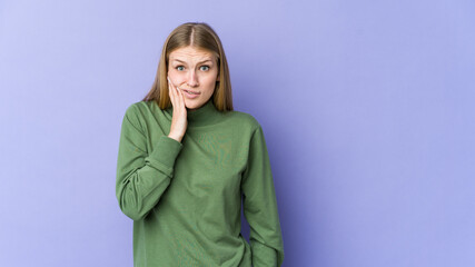 Young blonde woman isolated on purple background blows cheeks, has tired expression. Facial expression concept.