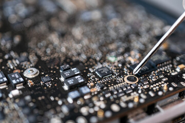 Repairing broken laptop computer mainboard, technician using  screwdriver.