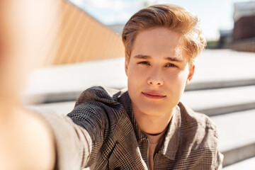 leisure, technology and people concept - nice young man or teenage boy taking selfie in city