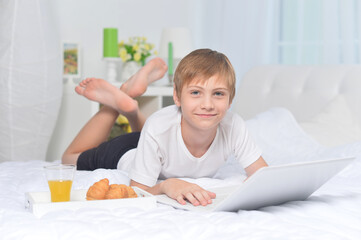 Obraz na płótnie Canvas Boy using laptop on bed while having breakfast