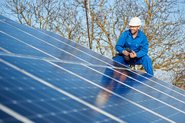 Smiling male engineer in blue suit and protective helmet installing photovoltaic panel system....