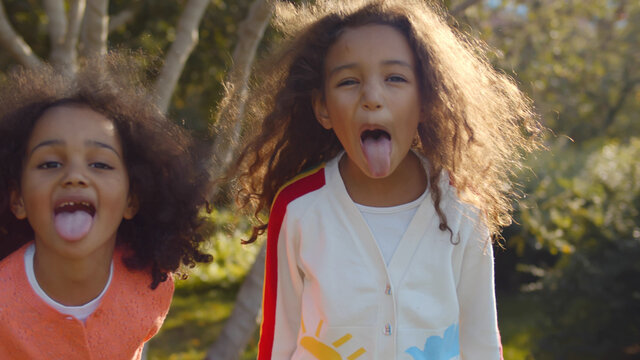 Portrait of adorable african girls making funny silly face showing tongue in park