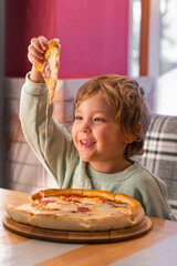 Cute boy eating a piece of pizza at fast food restaurant. Child unhealthy meal concept. Hungry kid