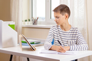Kid with digital tablet computer writing, doing homework at white desk. Online learning, remote education, distance lessons at home