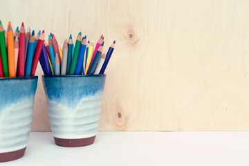 Colorful crayons in mug on white table with wooden background with copy space. Art and education in school and office. 