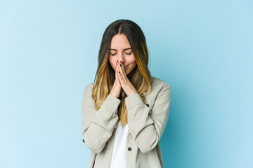Young caucasian woman isolated on blue background praying, showing devotion, religious person looking for divine inspiration.