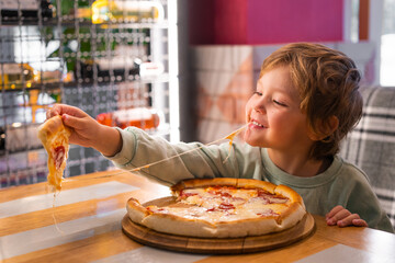 Cute boy eating a piece of pizza at fast food restaurant. Child unhealthy meal concept. Hungry kid