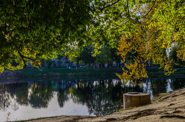 Landscape with autumn park in the sunny day. Yellow and green trees are displayed with reflection on the lake.