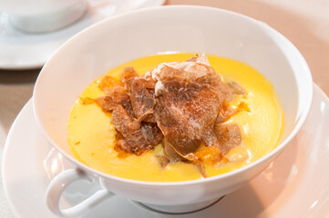 Alba white truffle sliced on delicious fontina cheese fondue in a white elegant ceramic cup with two handles on the saucer, close up