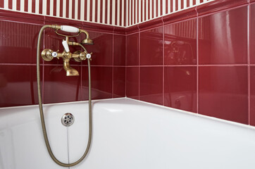 Modern bathtub with vintage mixer on the background of red tiles