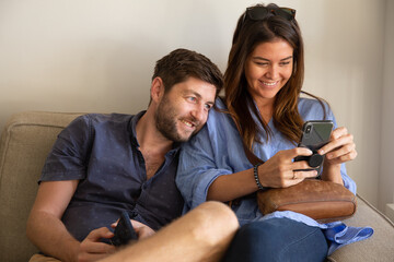 Young couple watching movie on cell phone and smiling on couch at living room