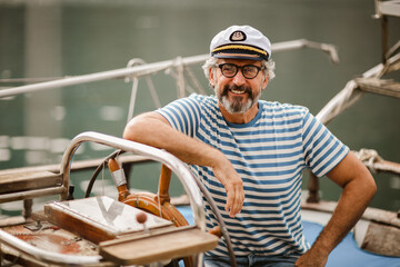 Mature man standing at helm of sailboat out at sea on a sunny afternoon.