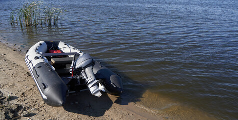 Inflatable boat with outboard motor on the sandy shore by river