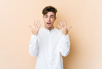 Young caucasian man isolated on beige background showing number ten with hands.