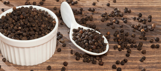 Piper nigrum - black peppercorns; photo on dark wooden background.