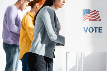voters in polling booths with american flag and vote inscription on blurred background