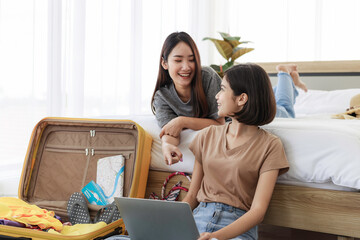 Two young asian women are using laptop to plan travel, book tickets, and booking accommodation online in bedroom. concept of travel in summer and holiday.