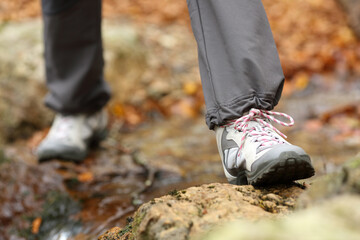 Trekker legs with boots crossing a river in autumn