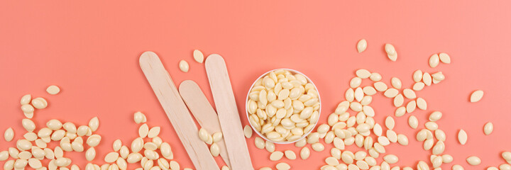 Wooden spatulas, depilation wax granules on pink background. Flat lay, beauty treatment concept....