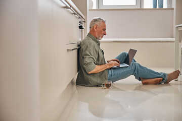 Fototapeta premium Barefoot senior citizen working on laptop at home