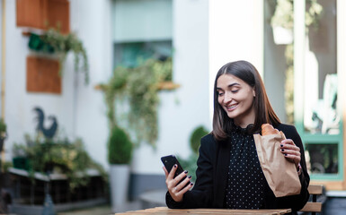 Young woman eating breakfast and smiling, eating croissants and talking on the phone. She is talking to someone on a cell phone. Breakfast.