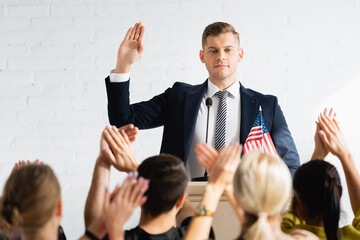 confident candidate showing swear gesture in front of applauding voters in conference room