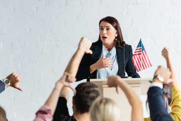 shocked political agitator in front of voters showing thumbs down in conference room, blurred...