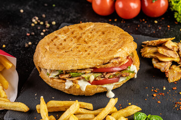 Turkish kebab in a fried bun with chicken, tomatoes, salad and cheese on a black background.