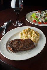 Steak dinner w/ vegetables. Traditional classical American or French Bistro main course, steak and mashed potatoes. Steak, cooked medium rare served with garlic mashed potatoes and kale salad.  