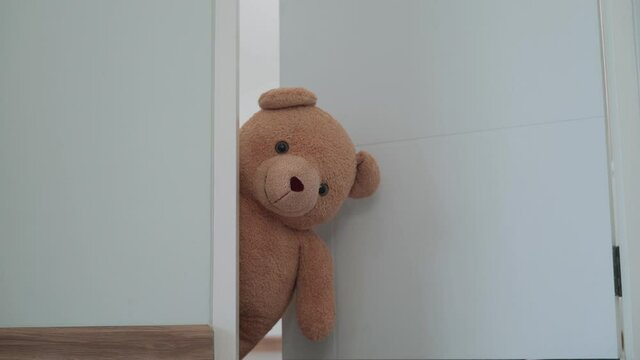 A brown teddy bear hidden inside the room near the door.A brown teddy bear poked his face from behind the wall...The brown teddy bear poke a face next to the door, the face of teddy bear look smiling.