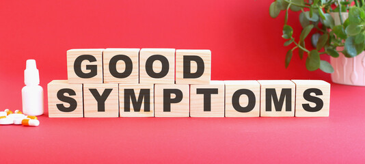 The words GOOD SYMPTOMS is made of wooden cubes on a red background. Medical concept.