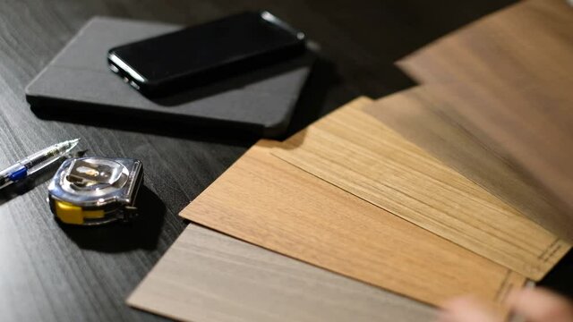 Selecting wood-grain laminate on a desk with a pen and a tape on the wooden table.