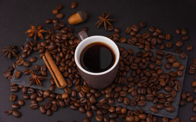A cup of espresso is decorated with anise stars, cinnamon, sweets, dried lemons, acorns, peanuts in a beautiful dish.