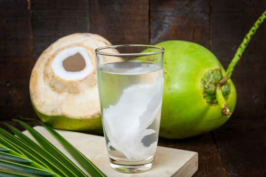 Fresh coconut juice in glass and coconut green leaf on wooden background.