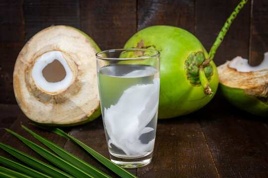 Fresh coconut juice in glass and coconut green leaf on wooden background.