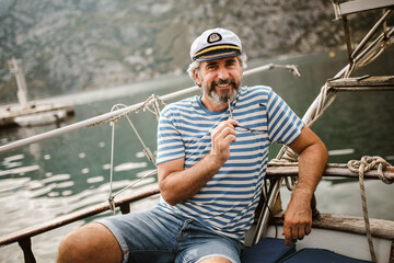 Mature man standing at helm of sailboat out at sea on a sunny afternoon.