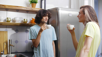 Gay couple at home in casual clothing drinking coffee in kitchen