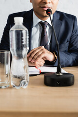 Cropped view of indian politician sitting near microphone with clenched hands on blurred foreground