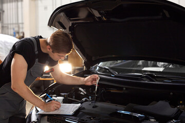 handsome caucasian guy is making notes while repairing hood of car, check all missing attributes...