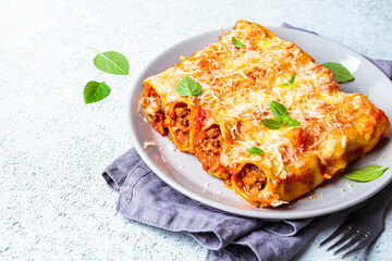 Portion of cannelloni with meat, tomato sauce and cheese on gray plate, gray background. Italian cuisine concept.